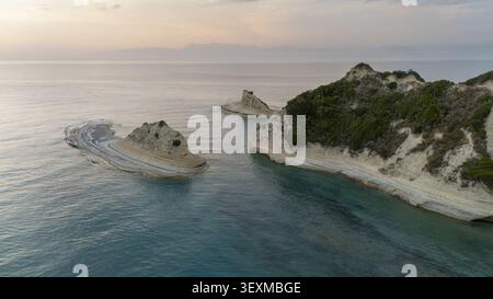 Blick aus der Vogelperspektive auf die dramatischen Kalksteinklippen von Kap Drastis, umgeben von türkisfarbenem Wasser und ruhigem Meer bei Sonnenuntergang in Korfu, Griechenland. Stockfoto