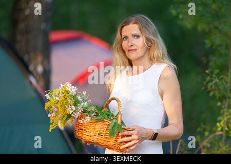 Eine Frau steht auf einem Campingplatz und hält einen Korb voller frischer Blumen. Stockfoto