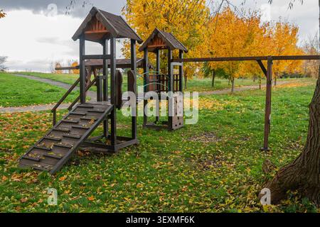 Hölzerne Spielplatzstruktur in einem Dorfhof, bedeckt mit bunten Herbstblättern Stockfoto