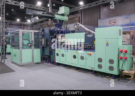 Bangkok, Thailand - 17. Juni 2026: Geschäftsmann beobachtet Spritzgießmaschine mit Roboterarm auf der Manufacturing Expo in Bangkok. Stockfoto