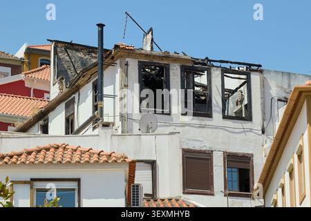 Verbrannte Wohnhausfassade mit zerstörtem Dach und gebrochenen Fenstern nach dem Brand. Stockfoto