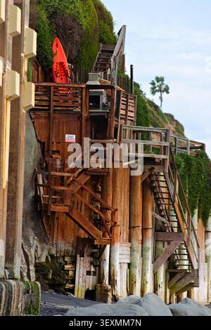 Holzdeck und Treppen entlang eines Küstenfeldes mit einem Surfbrett, das das Leben am Meer und den Zugang zur Küste in einem malerischen beac zeigt Stockfoto