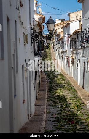 Eine typische Straße im historischen Zentrum von Altea, Alicante, Spanien, mit Ästen und Blättern auf dem Boden nach den Fronleichnamsfeiern Stockfoto