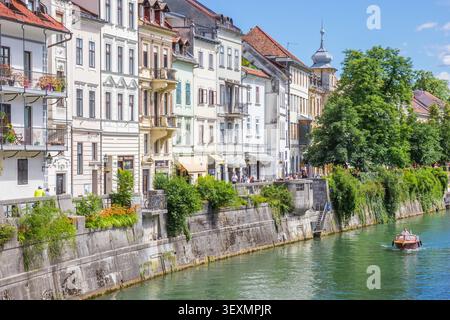 Der Fluss Ljubljanica fließt vorbei an farbenfrohen historischen Stadthausfassaden und einem kleinen Boot in Ljubljana, Slowenien Stockfoto
