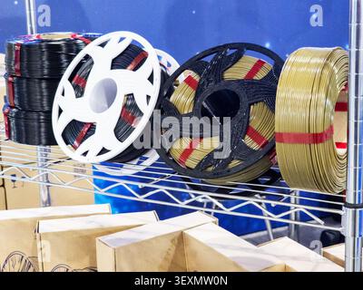 Mehrere Spulen und Spulen aus Kunststoff-Filament in Schwarz und Gold für den 3D-Druck auf einem Metallregal in einer Kreativwerkstatt oder einem Studio. Stockfoto
