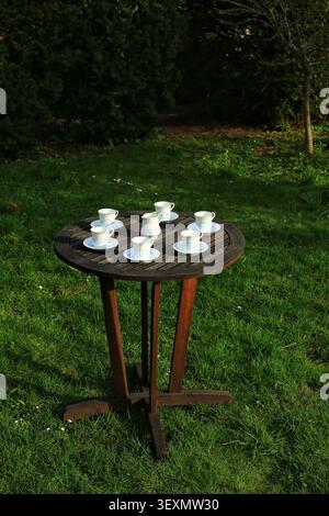 Gartentisch mit Holztisch und Porzellan-Kaffeetassen auf grünem Rasen. Stockfoto