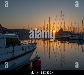 Loano Marina bei Sonnenaufgang. Sanft reflektiert im ruhigen Wasser, mit zahlreichen Booten und Yachten, die vertäut sind. Stockfoto