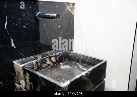Modernes Marmorwaschbecken mit wandmontiertem Wasserhahn in einem zeitgenössischen kommerziellen Toiletten. Premium-Badezimmer mit Innenausstattung und sanitären Designs für Büro und Öffentlichkeit Stockfoto