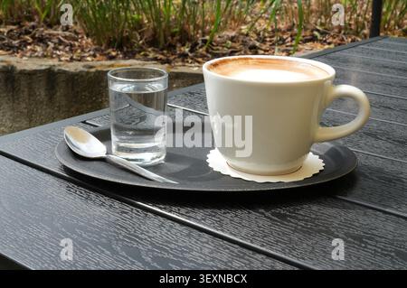 Tasse Kaffee auf einem Holztisch im Garten mit einem Glas Wasser Stockfoto