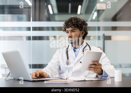 Ärztin im weißen Mantel und Stethoskop mit Laptop und digitalem Tablet, Verwaltung von Patientendaten oder Recherche medizinischer Informationen in einem modernen Klinikbüro Stockfoto