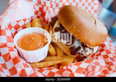 Nahaufnahme eines beladenen Burgers mit knusprigen Pommes und tauchenden Saucen auf einem rot karierten Picknicktisch Stockfoto