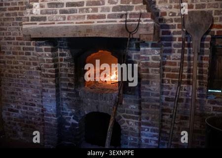 Rustikaler Backofen mit Holzofen und glühendem Feuer und traditionellen Backwerkzeugen in historischer Küche Stockfoto