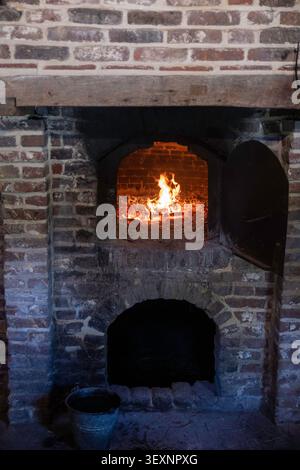 Rustikaler Backofen mit Holzofen und glühendem Feuer und traditionellen Backwerkzeugen in historischer Küche Stockfoto