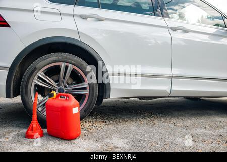 Kraftstoffbehälter und Ausgießtrichter neben dem geparkten Auto im Freien, bereit für das Betanken des Fahrzeugs. Konzept: Kraftstoffreserve Stockfoto