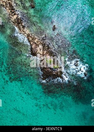 Blick aus der Vogelperspektive auf eine felsige Insel, umgeben von klarem türkisfarbenem Wasser mit sanften Wellen, die gegen die Küste in Phuket, Thailand, brechen. Stockfoto