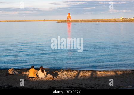 Paar sitzt am Strand bei Sonnenuntergang Stockfoto