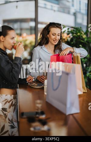 Zwei Freundinnen packen bunte Geschenktüten in einem Café während eines fröhlichen Treffens aus Stockfoto