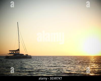 Silhouettenkatamaran segeln auf dem ruhigen Ozean bei Sonnenuntergang Stockfoto