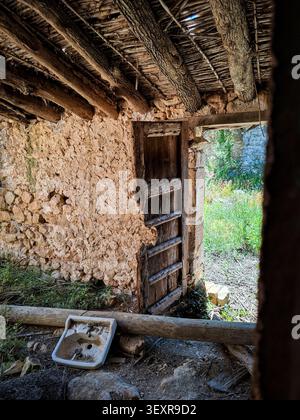 Innenansicht zeigt ein verlassenes mittelalterliches maurisches Haus in Vall de Ebo, Spanien. Eine kaputte Holztür steht offen und ein altes Waschbecken liegt auf dem Boden Stockfoto