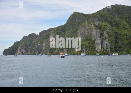 Phi Phi Inseln, Thailand – 18. Mai 2026: Boote vor Anker in der Bucht, umgeben von hohen Kalksteinklippen und tropischer Küste auf den Phi Phi Inseln Stockfoto