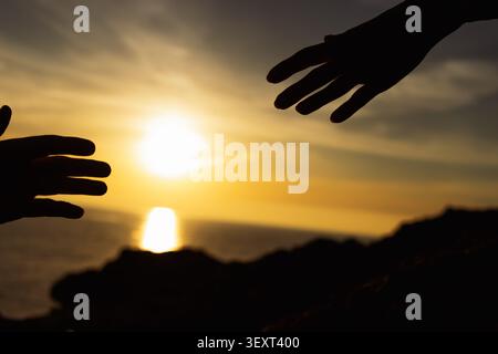 Silhouetten aus zwei Händen reichen zueinander. Symbolisiert die Verbindung. Hilfe. Und Partnerschaft. Vor einem dramatischen goldenen Sonnenuntergang, der sich auf Th reflektiert Stockfoto