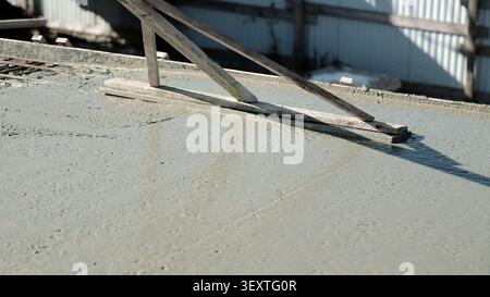 Nasse Betonplatte Mit Holzestrich Nivelliert. Nasse Betonplatte wird mit einem Holzestrich auf einer sonnendurchfluteten Baustelle mit Schalungskanten nivelliert Stockfoto