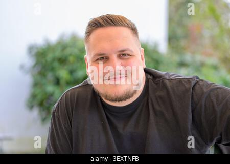 Freundlicher junger Mann, der selbstbewusst in die Kamera schaut, während er legere schwarze Kleidung in einer entspannten Umgebung trägt. Authentisches Lifestyle-Porträt mit n Stockfoto