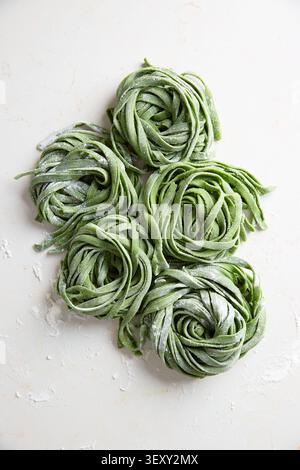 Grüne hausgemachte Pasta nestet mit Mehl auf weißer Oberfläche, traditionelle italienische Zubereitung Stockfoto