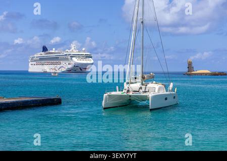 Ein Katamaran-Segelboot, das im klaren türkisfarbenen Karibischen Meer entlang der felsigen tropischen Uferpromenade von George Town in den Cayman Islands Vacation des vor Anker geht Stockfoto