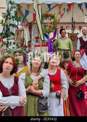 Tallinn, Estland - 7. Juli 2022: Gruppe in mittelalterlichen Kostümen mit Blumenkränzen posiert unter einem verzierten Zelt mit heraldischen Fahnen, mittelalterliche Tage Stockfoto