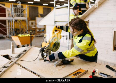 Fokussierte junge Studentin mit Gehrungssäge Holz an Werkbank im Berufszentrum Stockfoto