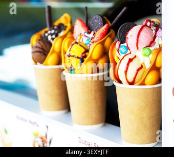 Luftige Waffeln mit verschiedenen süßen Füllungen, Oreos, Schokolade, Marshmallows, Obst, in Pappbechern. Stockfoto