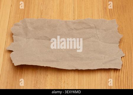 Leeres, zerknittertes braunes Kraftpapierblatt auf Holzschreibtisch, ideal für Vintage-Design und Recyclingpapierkonzepte Stockfoto