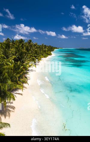Blick von oben nach unten auf Dhigurah Island, Malediven, mit weißem Sand, der sich zwischen Palmen und einer türkisfarbenen Lagune windet, Korallenflecken sichtbar, sanfte Wa Stockfoto
