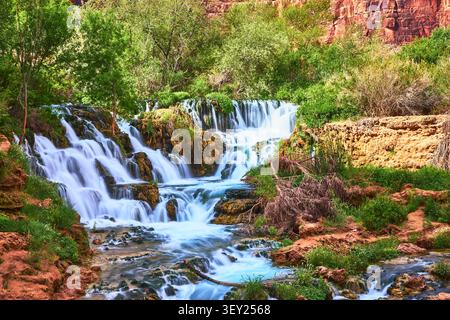 Wasserfall, der über moosige Felsen fließt, mit üppiger Vegetation und roten Klippen in Arizona Stockfoto