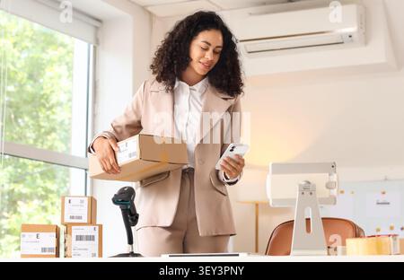 Frau mit Paket und Smartphone im Büro Stockfoto