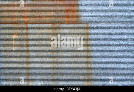 Nahaufnahme von verwitterten überlappenden, galvanisierten gewellten Metallplatten mit horizontalen Graten, Roststreifen von der oberen Platte Stockfoto