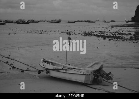 Phi Phi Inseln, Thailand – 18. Mai 2026: Ein kleines Motorboot ruht bei Ebbe an der freiliegenden Sandküste, mit traditionellen thailändischen Langboot-Booten vor Anker Stockfoto