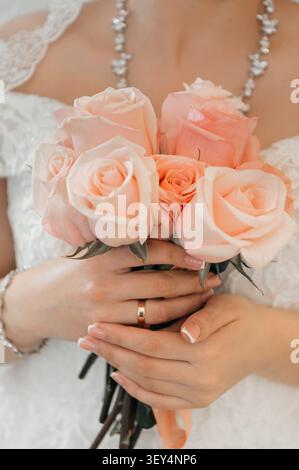 Nahaufnahme einer Braut in einem weißen Spitzenkleid mit einem wunderschönen Blumenstrauß aus rosa Rosen, die ihren eleganten goldenen Ehering und einen französischen Mann zeigt Stockfoto