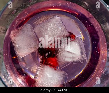 Eiswürfel, die in einem Glas aus rosa Gin mit sichtbaren Blasen schweben Stockfoto