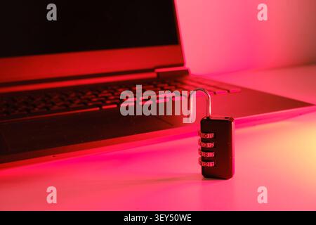 Entsperrtes Kombinationsvorhängeschloss, das die Cybersicherheit auf einem Laptop in rotem Licht symbolisiert Stockfoto