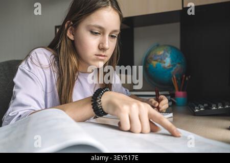 Das Mädchen macht aktiv Notizen in einem Notizbuch für die Hausaufgaben, während es in ihrem Zimmer sitzt Stockfoto