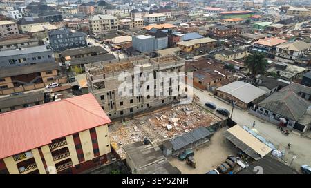 Luftaufnahme einer Baustelle mit einem mehrstöckigen Gebäude in der Entwicklung, umgeben von dichten städtischen Wohnhäusern und Straßen in Lagos, L Stockfoto