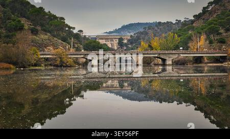 Herbstblick vom Erholungsgebiet La Depuradora auf dem Fluss Alberche mit Brücke San Juan im Hintergrund, in der Nähe von Pelayos de la Presa, Madrid, Spanien Stockfoto