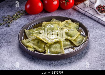 Grüne Ravioli mit Olivenöl auf dunkler Keramikplatte. Thymian aus frischen Tomaten im Hintergrund. Weiche Beleuchtung hebt die Textur hervor. Erdtöne mit r Stockfoto
