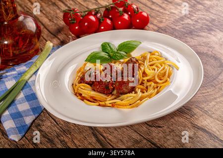 Appetitliche Spaghetti-Fleischbällchen-Teller mit vibrierender roter Sauce, frischen grünen Basilikumblättern. Serviert auf rustikalem Holzhintergrund, ergänzt durch Kirschtomate Stockfoto