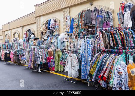 Farbenfrohe traditionelle Kleidung und Textilien auf Regalen vor dem Siab Basar in Samarkand. Farbenfrohe Ikat-Bademäntel, bestickte Kleidungsstücke und Schals Stockfoto