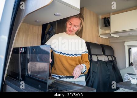 Junge Frau kocht Frühstück in der modernen Wohnmobilküche während eines Roadtrip-Abenteuers Stockfoto