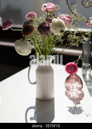 Elegantes Blumenarrangement mit farbenfrohen Ranunkelblüten, beleuchtet durch natürliches Fensterlicht Stockfoto