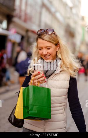 Frau lächelt, hält Einkaufstaschen und Smartphone draußen Stockfoto